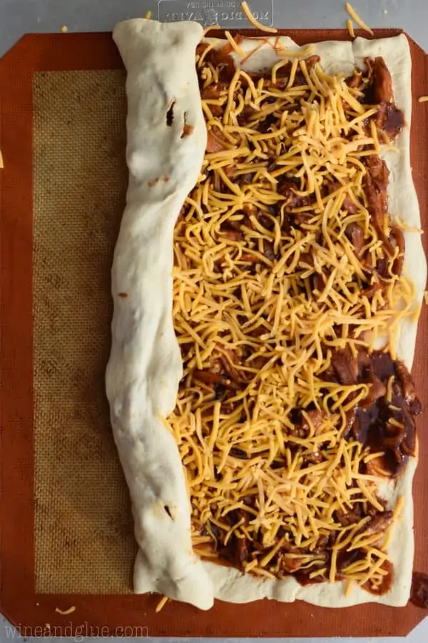 The uncooked BBQ Chicken Pizza Roll is being rolled up on the baking sheet. 