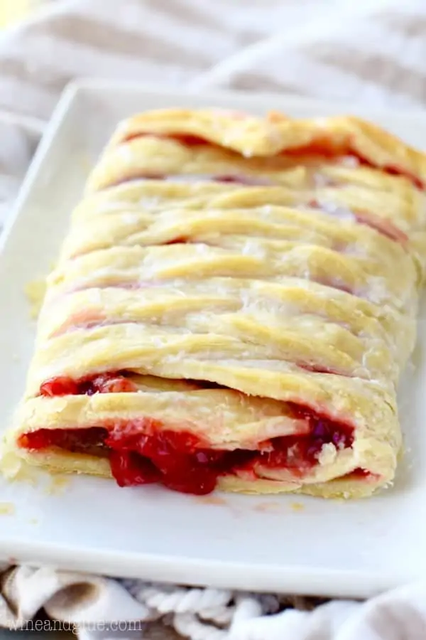 On a white plate, the Cherry Almond Braid has some cherry filling oozing and glazed with some icing. 