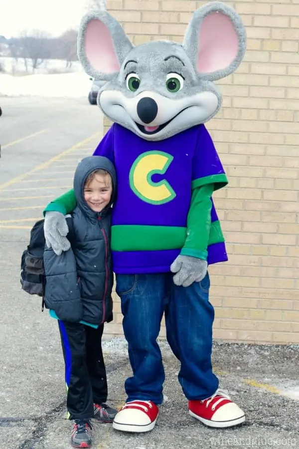 A little boy taking a picture next to Chuck E. Cheese. 