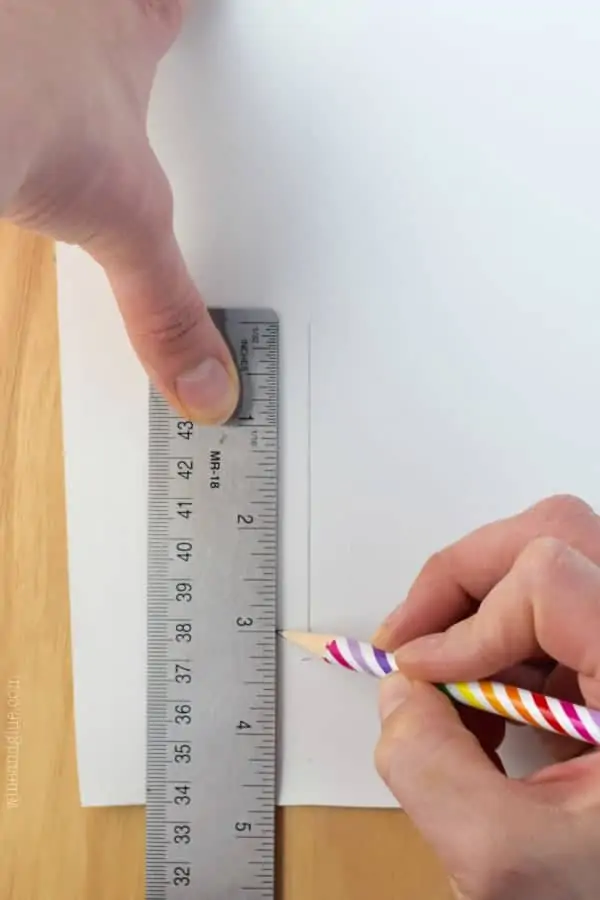 On a piece of paper, a woman holding a ruler and making a line with a pencil. 