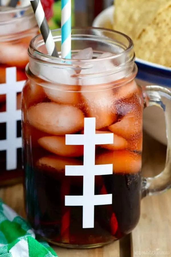 In a mason jar glass looking like a football, the Super Bowl Slammer has cubed ice in it with two paper straws. 