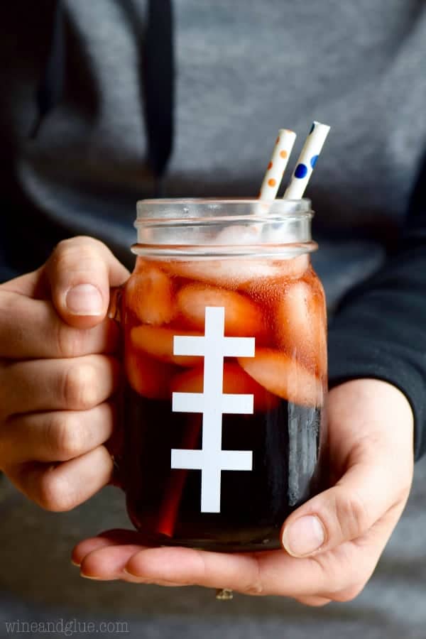 A woman holding the Super Bowl Slammers in a mason jar with one vertical line and three horizontal lines making the glass look like a football. 