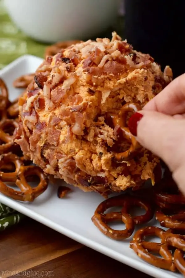 A woman digging into the Buffalo Bacon Cheeseball with a pretzel. 