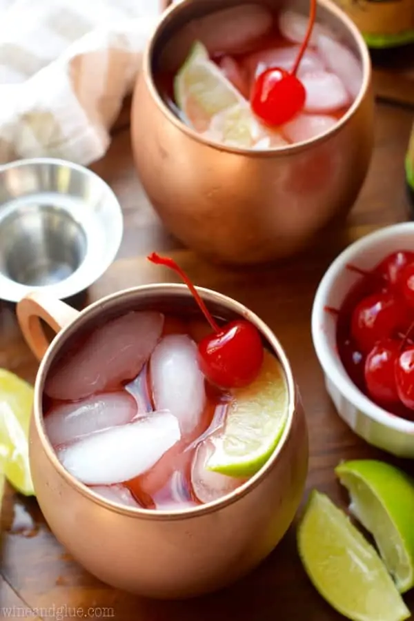 In copper mugs, the Cherry Moscow Mules has cubed ice, red tint, a maraschino cherry, and a sliced lime. 