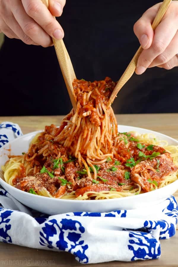 On a white bowl, a wooden spoon and fork are picking up some the French Spaghetti that is topped with parsley and parmesan cheese.  