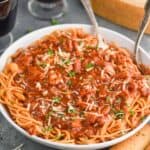 a large white serving bowl full of chicken spaghetti - a spaghetti with red sauce and shredded chicken garnished with parsley and fresh parmesan