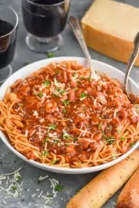 a large white serving bowl full of chicken spaghetti - a spaghetti with red sauce and shredded chicken garnished with parsley and fresh parmesan