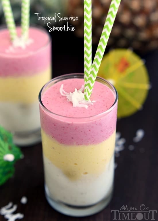 In a cylindrical glass, the Topical Sunrise Smoothie has distinct layers of white, pastel yellow, and pastel red and topped with coconut shreds. 