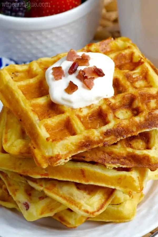 Stacked high, the Bacon Cheddar Sour Cream Waffles has a golden brown color and topped with a dollop of sour cream and minced bacon. 