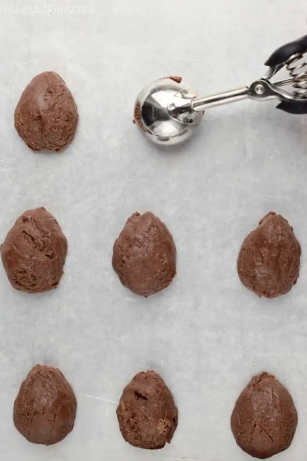 The creamy chocolate fudge is being scooped on a parchment paper with the ice cream scooper then being shaped into little eggs. 