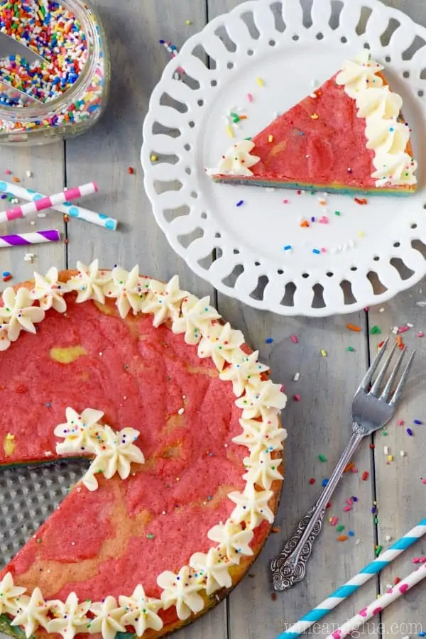 An overhead photo of the Rainbow Sugar Cookie Cake with a slice cut out and next to the cake on a white plate. 