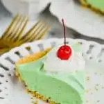 piece of green shamrock shake pie on a white plate topped with whipped cream and a cherry