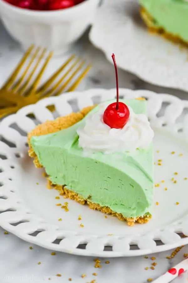 piece of green shamrock shake pie on a white plate topped with whipped cream and a cherry