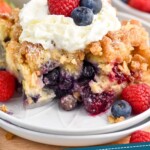 Pinterest graphic for Berry French Toast Casserole recipe. Image is close up photo of a piece of Berry French Toast Casserole served on a plate and garnished with whipped cream and berries. Bowl of berries and cup of coffee in the background. Text says, "overnight berry french toast casserole simplejoy.com"