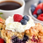 Pinterest graphic for Berry French Toast Casserole recipe. Text says, "amazing Berry French Toast Casserole simplejoy.com." Image is close up photo of a piece of Berry French Toast Casserole garnished with berries and whipped cream. Cup of coffee and bowl of berries in the background.