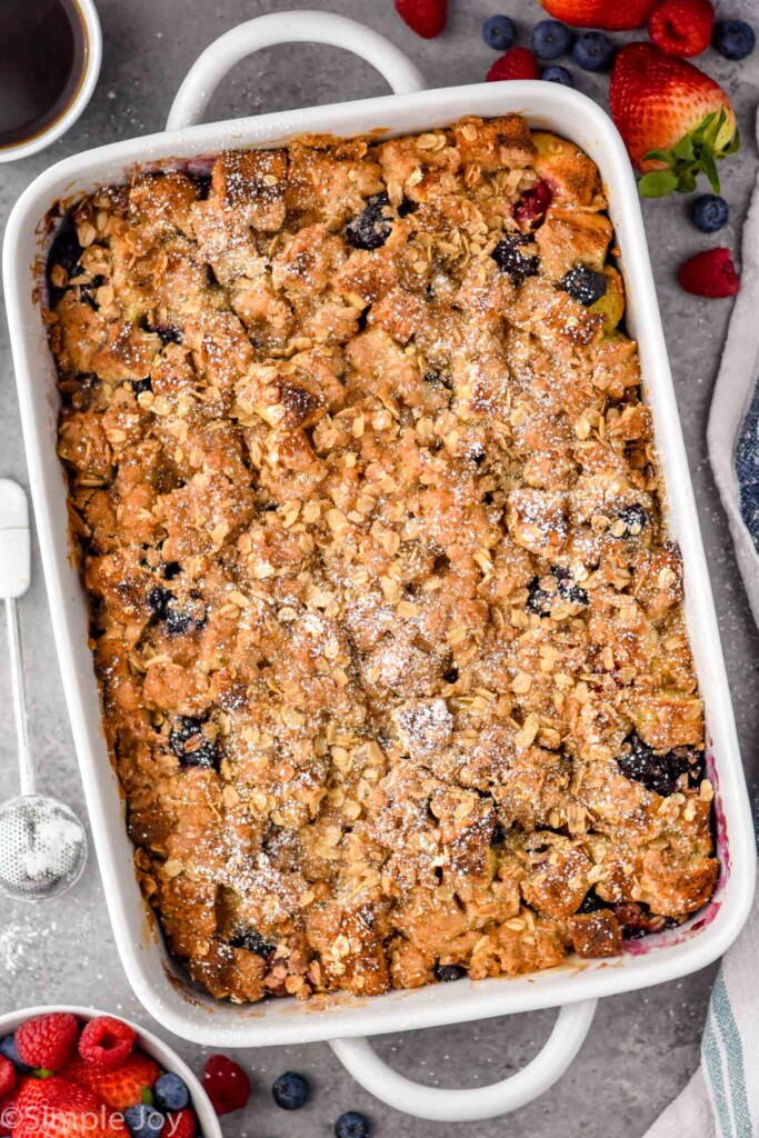 Overhead photo of a baking dish of Berry French Toast Casserole recipe. Extra berries on counter beside baking dish.