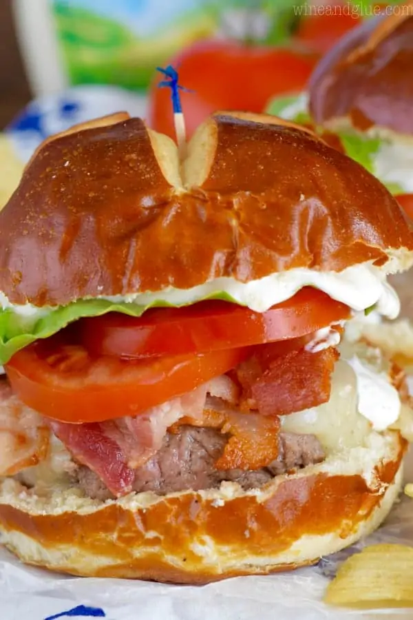 In between two pretzel buns, the BLT Ranch Burger has lettuce, tomato, bacon, melted cheese, a burger patty, and ranch oozing out.
