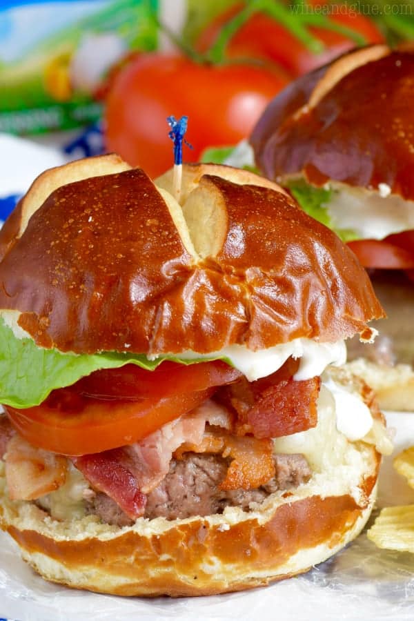 In between two pretzel buns, the BLT Ranch Burger has lettuce, tomato, bacon, melted cheese, a burger patty, and ranch oozing out.