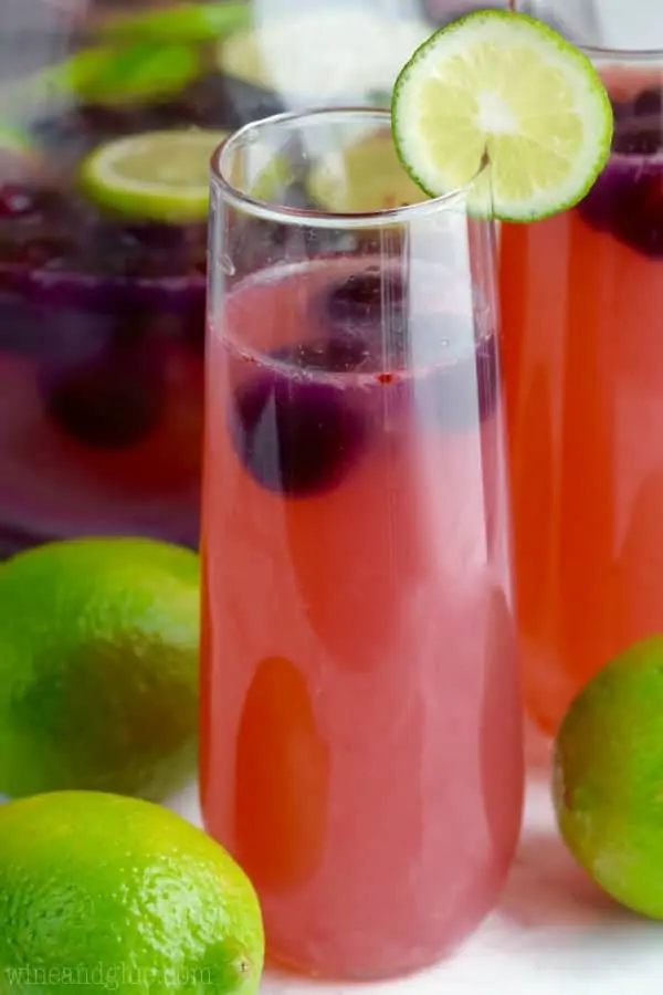 The Cherry Limeade Sangria has a pink red tint has some black cherries floating in the drink with a slice lime on the rim. 