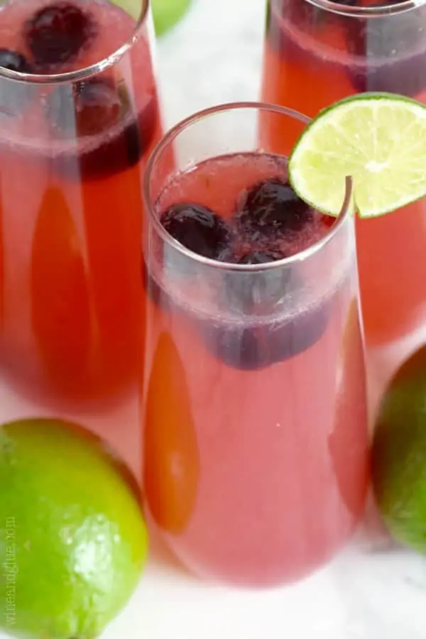 The Cherry Limeade Sangria has a pink red tint has some black cherries floating in the drink with a slice lime on the rim. 