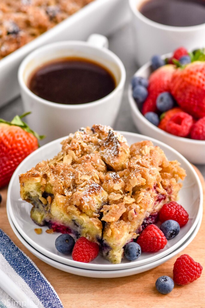 Photo of a piece of Berry French Toast Casserole served on a plate garnished with extra berries. Cup of coffee and bowl of berries on counter.