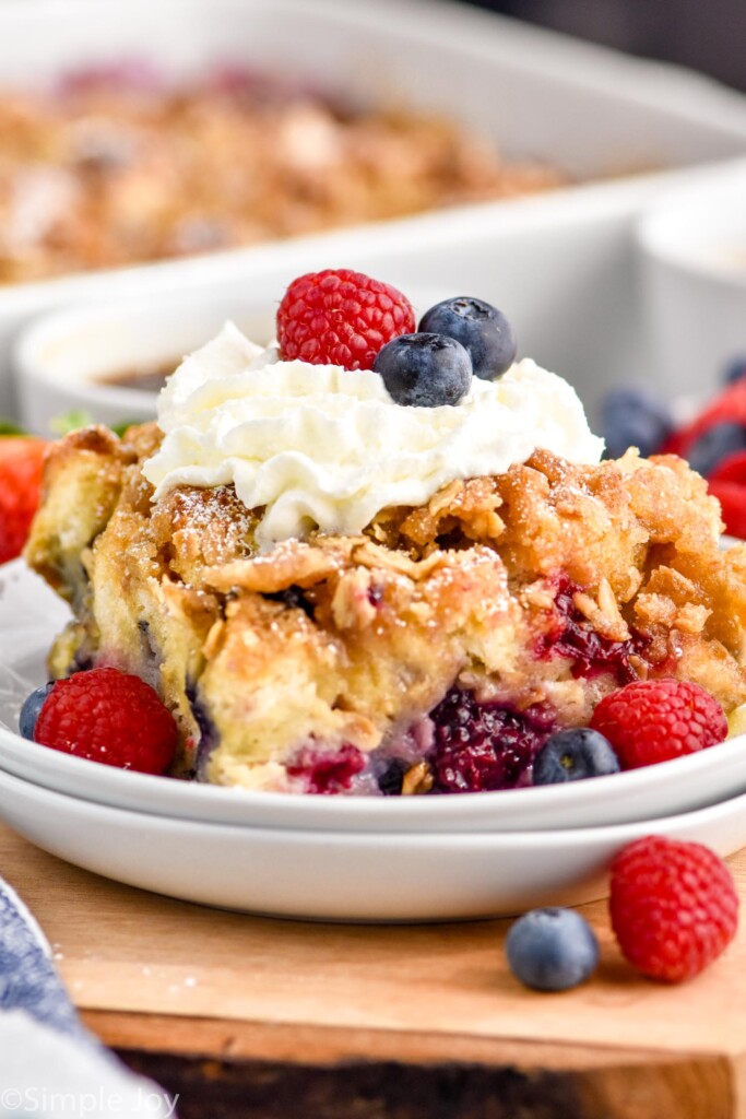 Close up photo of a piece of Berry French Toast Casserole served on a plate garnished with berries and whipped cream.