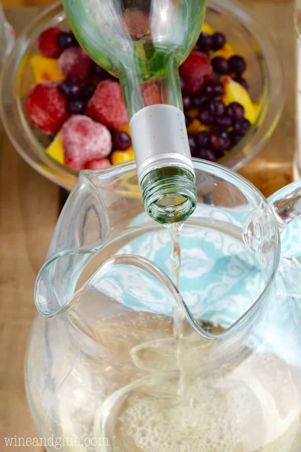 A bottle of white wine is being poured into a large pitcher. 