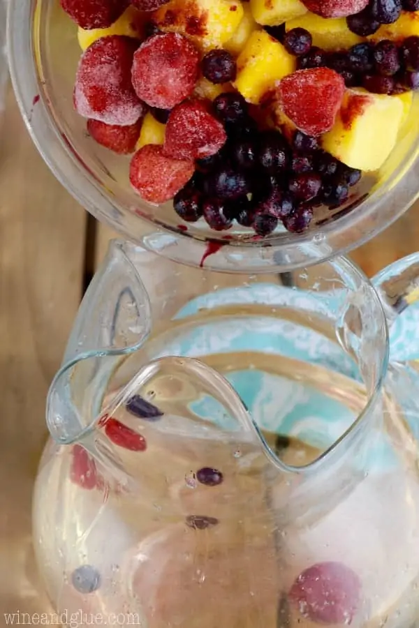 A large bowl of frozen fruit is poured into the pitcher. 
