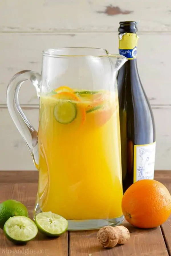 In a large pitcher, slices of limes and oranges float in an orange liquid called the Mimosa Margaritas. 