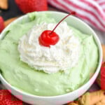 bowl of green pistachio cheesecake dip topped with whipped cream and a cherry - 13