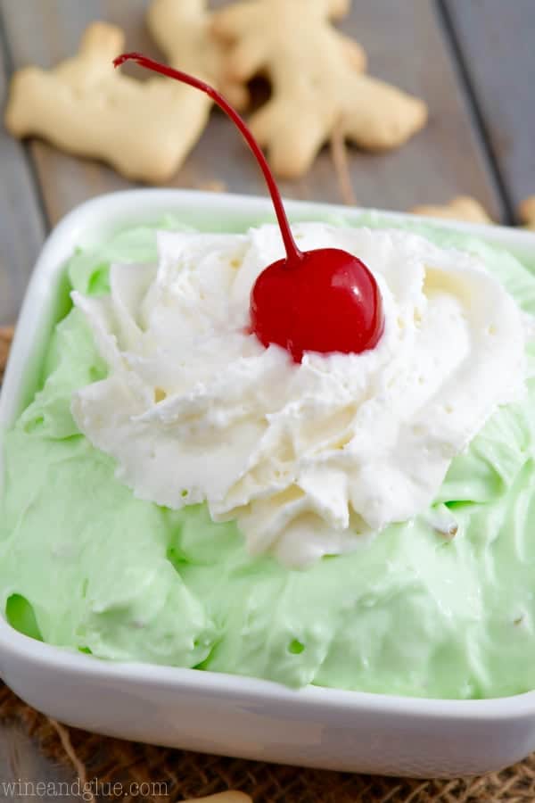 The Pistachio Cheesecake Dip has a fluffy texture with a lime green color and topped with whipped cream and a single cherry. 