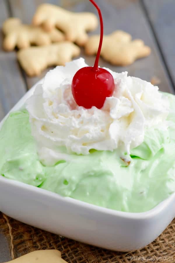 The Pistachio Cheesecake Dip has a fluffy texture with a lime green color and topped with whipped cream and a single cherry. 