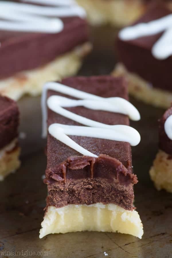 A large bite in the Sugar Cookie Fudge Bars showing the distinct layers of the cookie, fudge, chocolate, and the white zig zag frosting. 