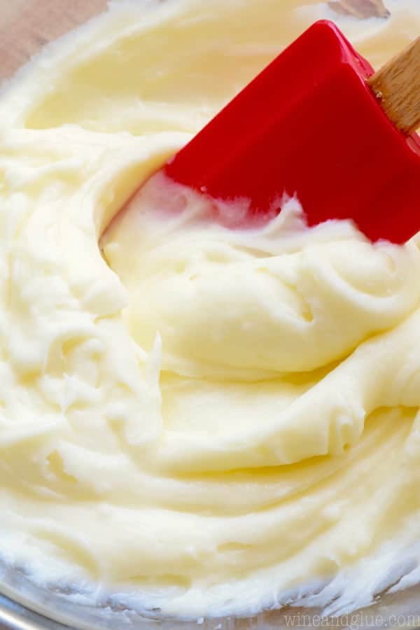 red spatula dipping into a bowl of cream cheese frosting