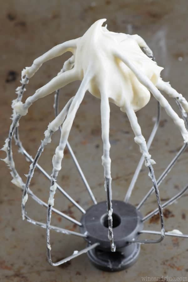 the whisk attachment of a kitchen aid mixer sitting on a gray surface with cream cheese frosting on it