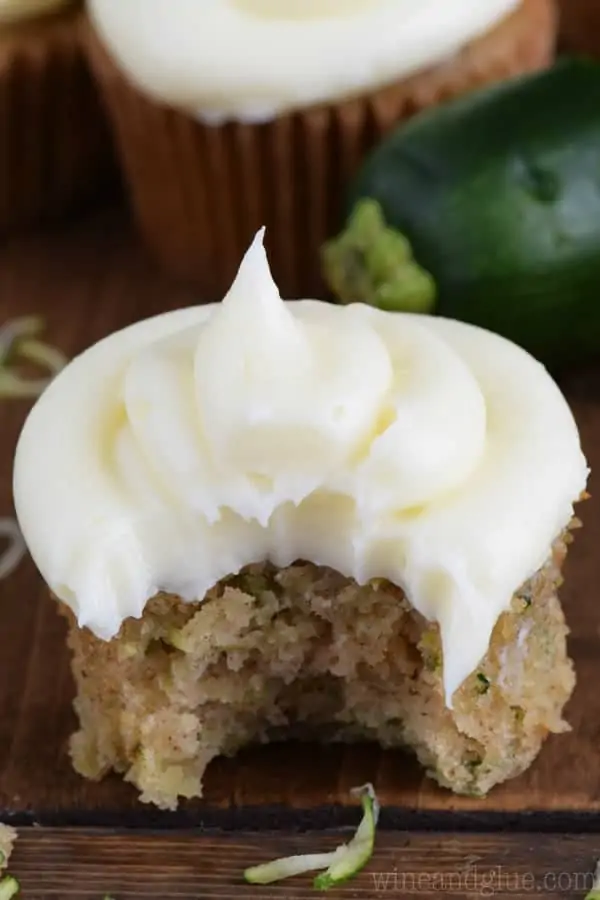 A large bite out of the Zucchini Cupcake showing the golden brown interior with a fluffy cream cheese frosting on top. 