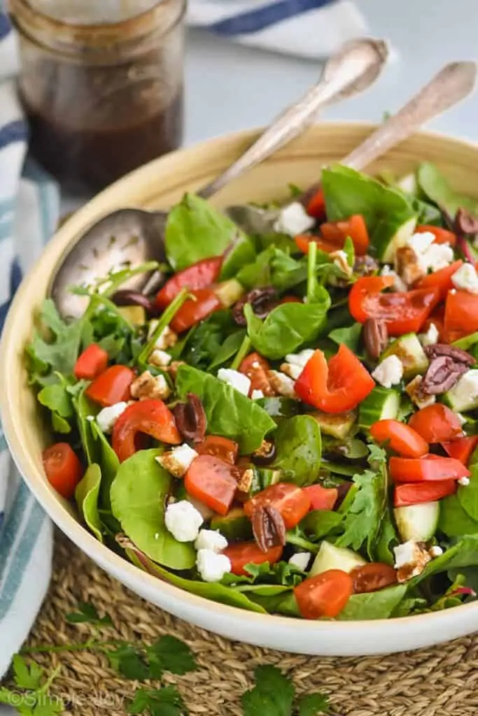 a mixed green salad with red peppers, feta cheese, kalamata olives, and tomatoes tossed with balsamic vinaigrette dressing