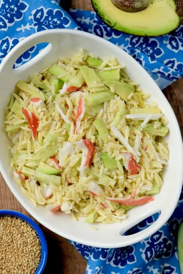 In a white bowl, slices of avocado and crab meat has been mixed within the Orzo Pasta and topped with white sesame seeds. 