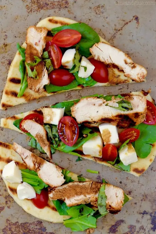 Three pieces of Grilled Capese Flat Bread topped topped with basil, grilled chicken, cherry tomatoes, and mozzarella. 