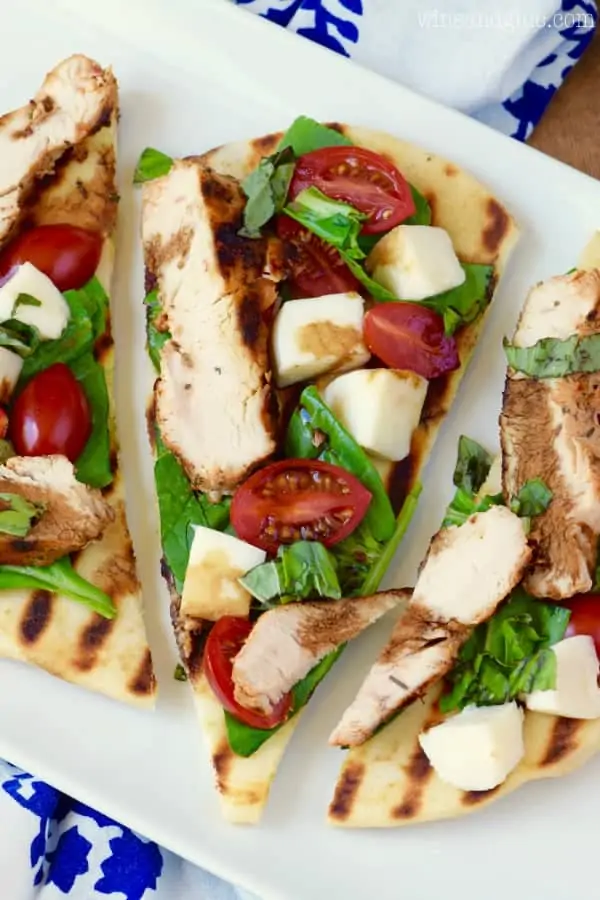 An overhead photo, three Grilled Chicken Capese Flatbread showing the grilled chicken, halved cherry tomatoes, cheese, and basil. 