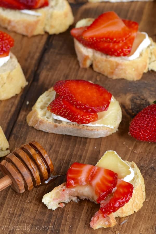 On a slice of baguette, a slice of Brie is topped with two thin slices of strawberry and honey is drizzled on top to make the Honey, Strawberry, and Brie Bruschetta. 