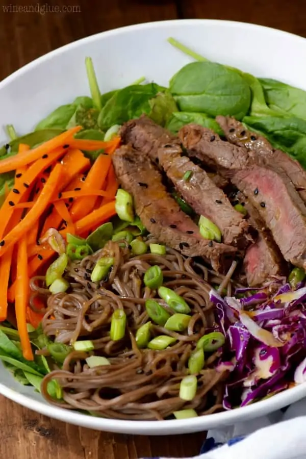 An overhead photo of a bowl of the Soba Noodle Steak Salad that has spinach, carrots, sliced steaks, red cabbage, soba noddles, and topped with black sesame seeds and scallions. 