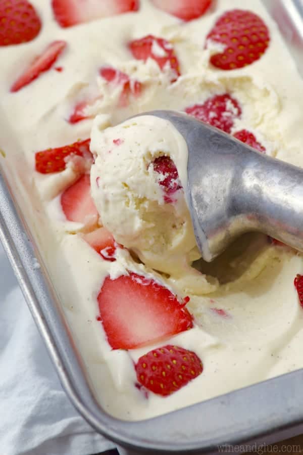 In a bread pan, an ice cream scooper is getting a scoop of the Strawberries and Cream Ice Cream. 