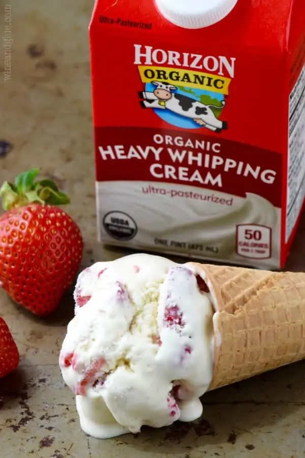 A scoop of Strawberry and Cream Ice Cream in a waffle cone in front of Horizon Organic Heavy Whipping Cream. 