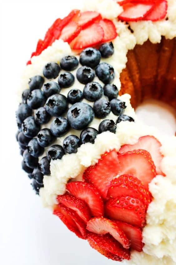 The Red White and Blue Bundt Cake has distinct strips of cut strawberries, blueberries, and pipped vanilla frosting. 