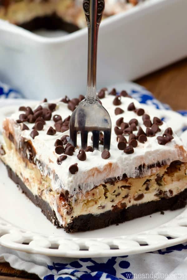 On a white plate, the Cookie Dough Lush has distinct layers of an Oreo crust, cookie dough, and frosting topped with mini chocolate chips.