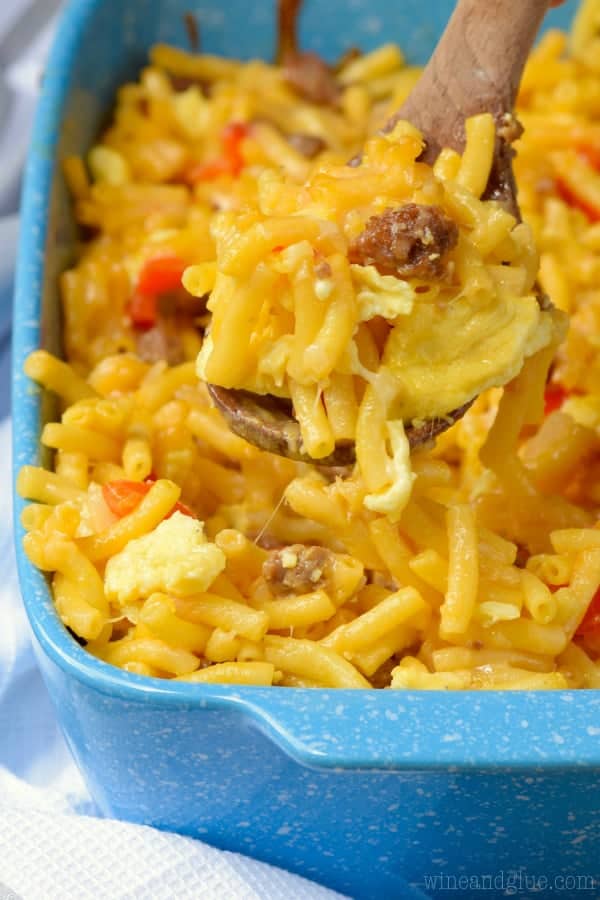 In a blue casserole dish, the Mac N' Cheese Breakfast Casserole has chunks of sausage, Mac and Cheese, eggs, and sliced red peppers. 