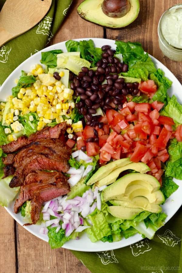 An overhead photo of the Southwestern Steak Salad with Jalapeño Ranch Dressing showing the different toppings of steak, corn, black beans, avocado, red onion, and tomatoes. 