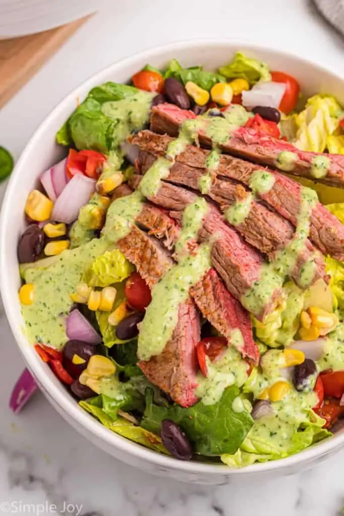 close up of a steak salad in a white bowl with dressing drizzled over the top