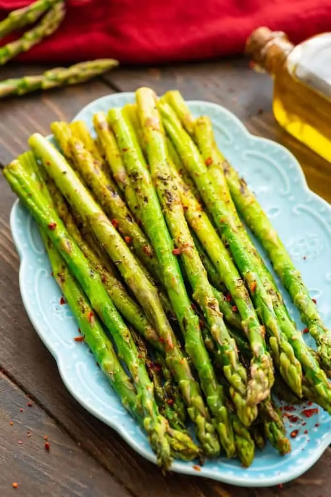 The Grilled Asparagus are on a blue platter topped with pepper. 